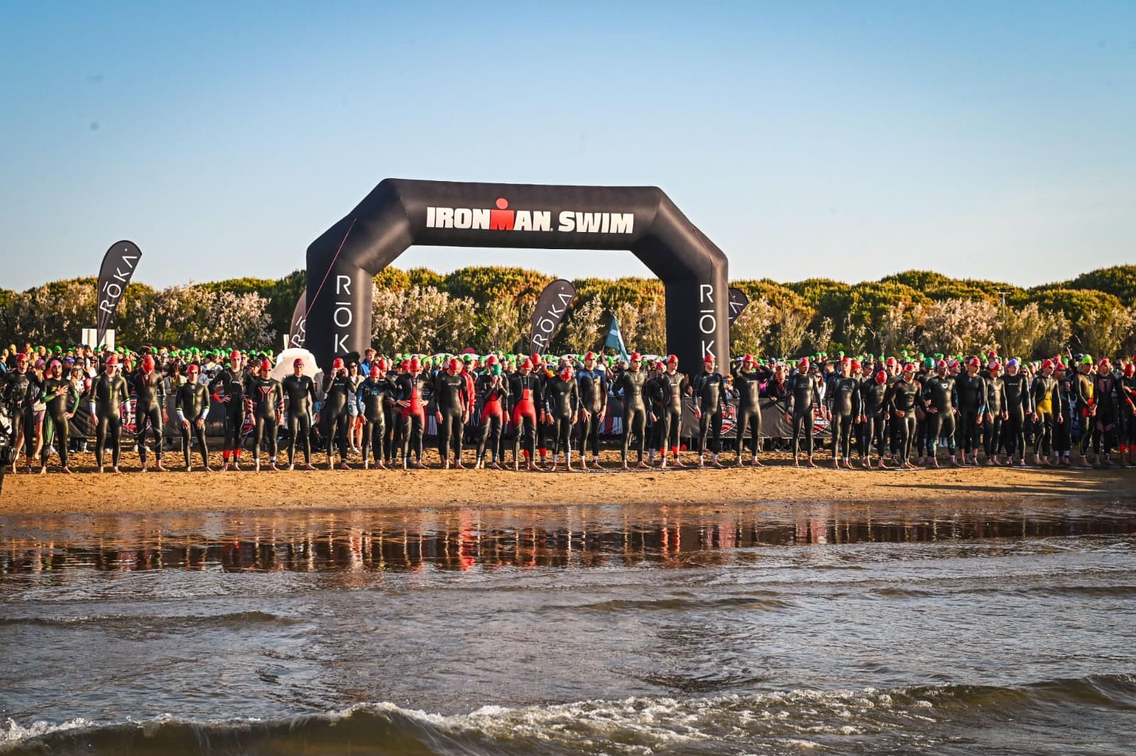 Athletes in wetsuits lined up on the beach at an Ironman swim start